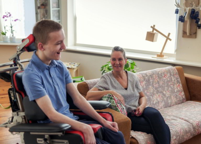 Disabled young man in a wheelchair smiling and talking with a woman sitting on a couch